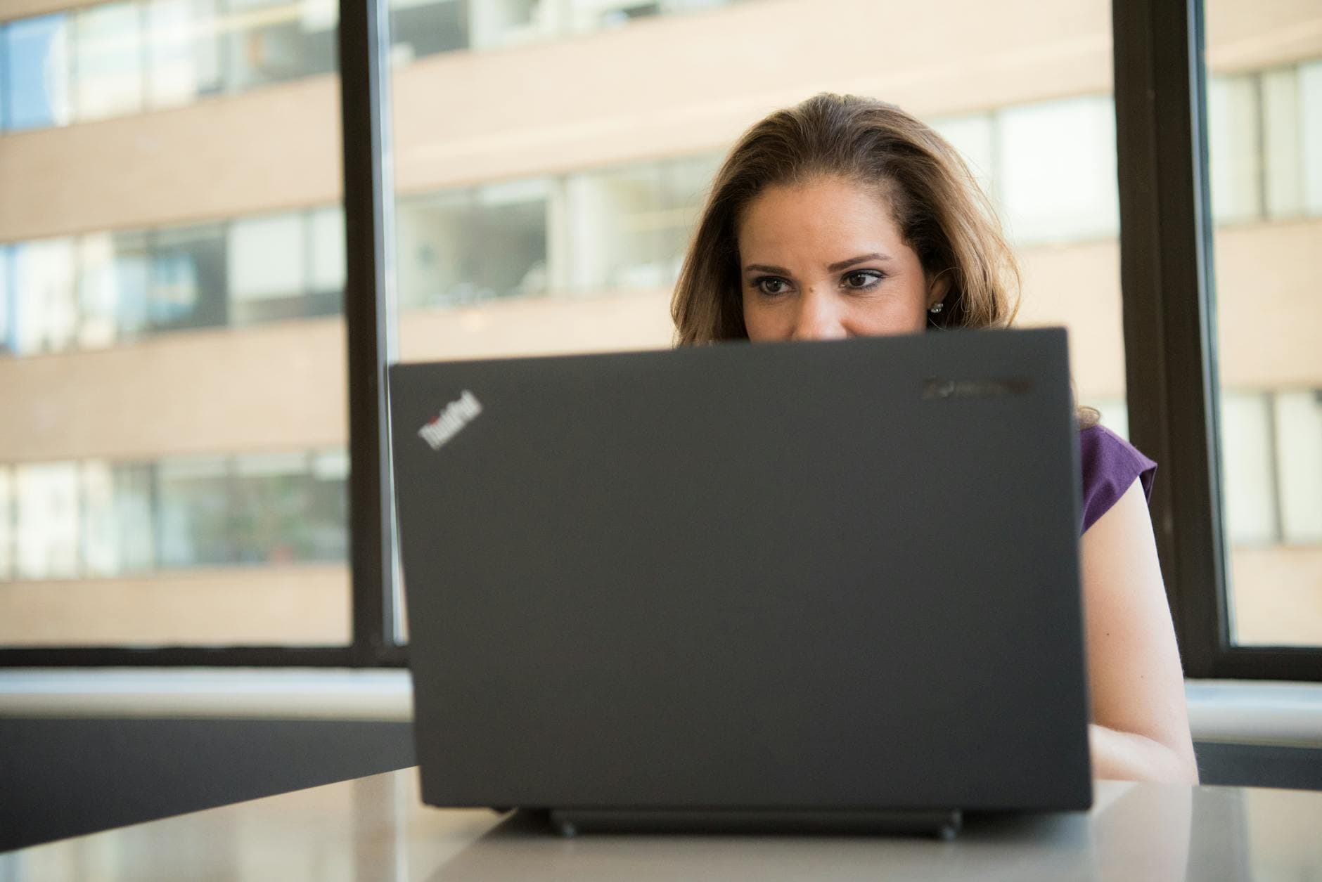 Focused woman working on laptop in a brightly lit office, optimizing her resume for ATS systems